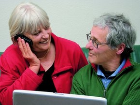[Translate to UK - englisch:] Elderly couple on front f a laptop looking at each other while she is talking on the phone
